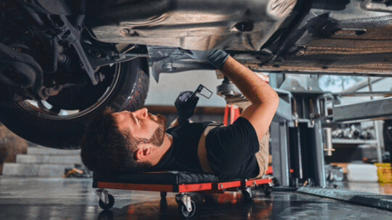 Mechanic lying under a car in workshop, checking and repairing vehicle parts during maintenance